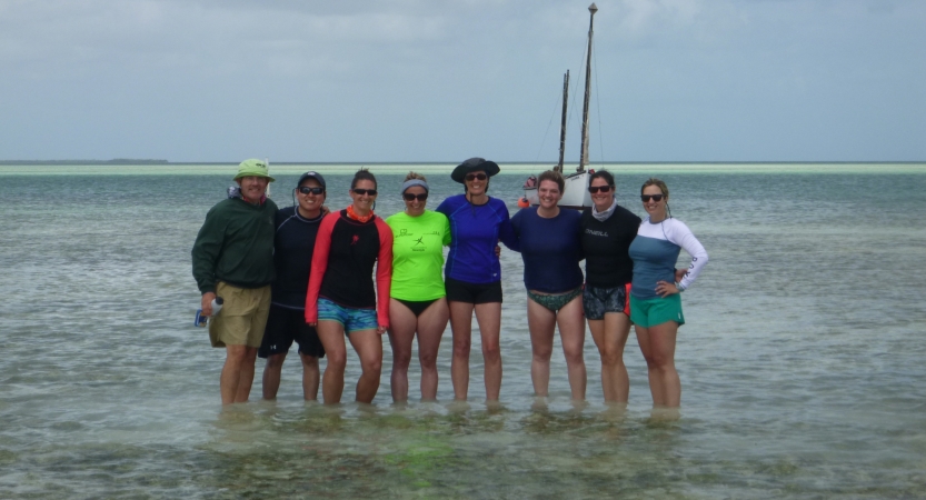 A group of people stand in ankle-deep water and smile for a group photo